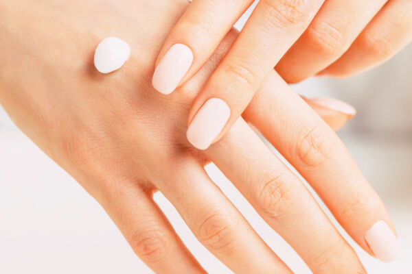 Young female hands with manicure of beige natural color applying moisturizing cream, concept of skincare and beauty.